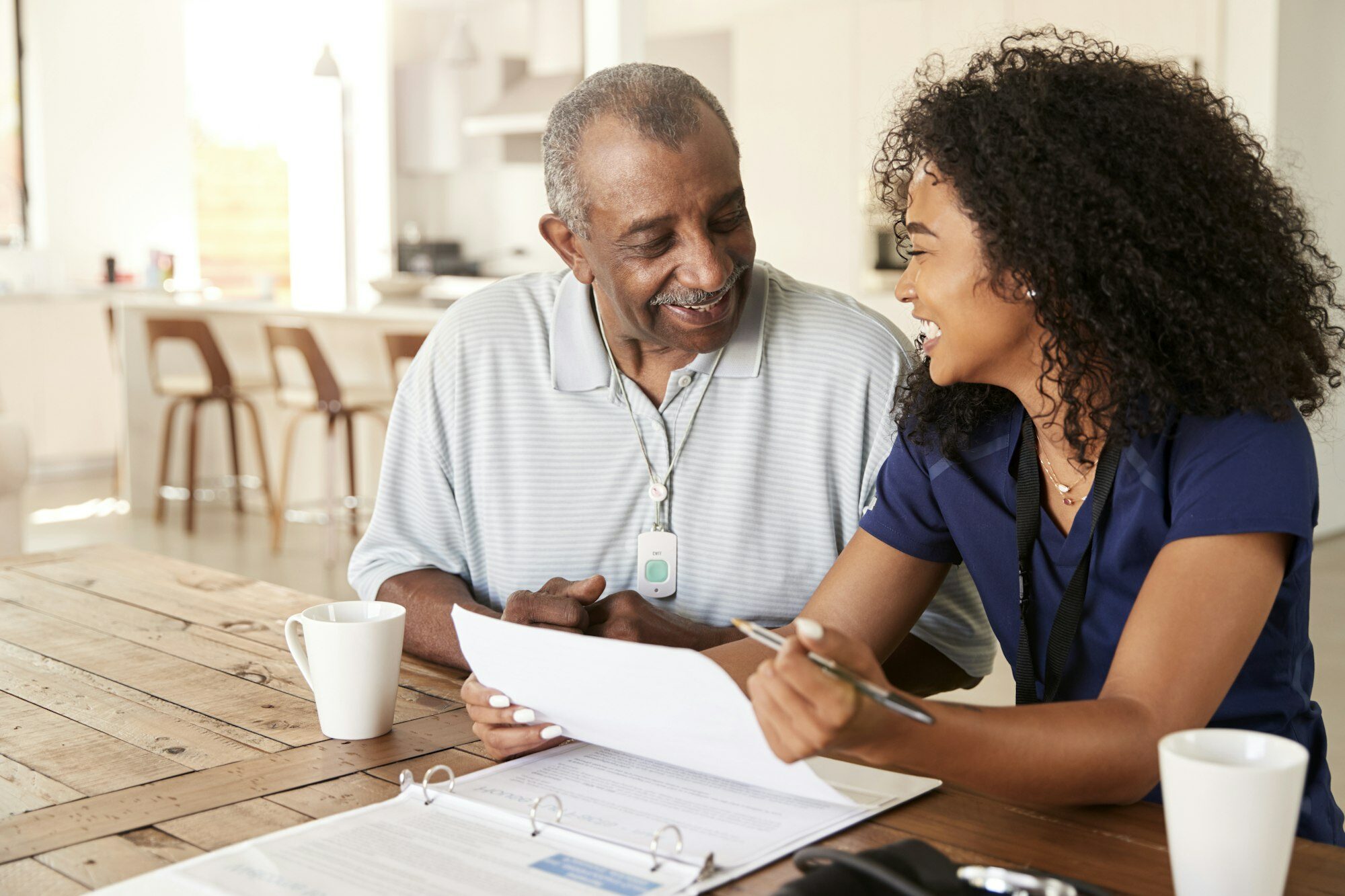 Happy female healthcare worker sitting at table smiling with a senior man during a home health visit
